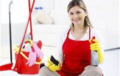 A woman holding cleaning supplies and a cell phone.